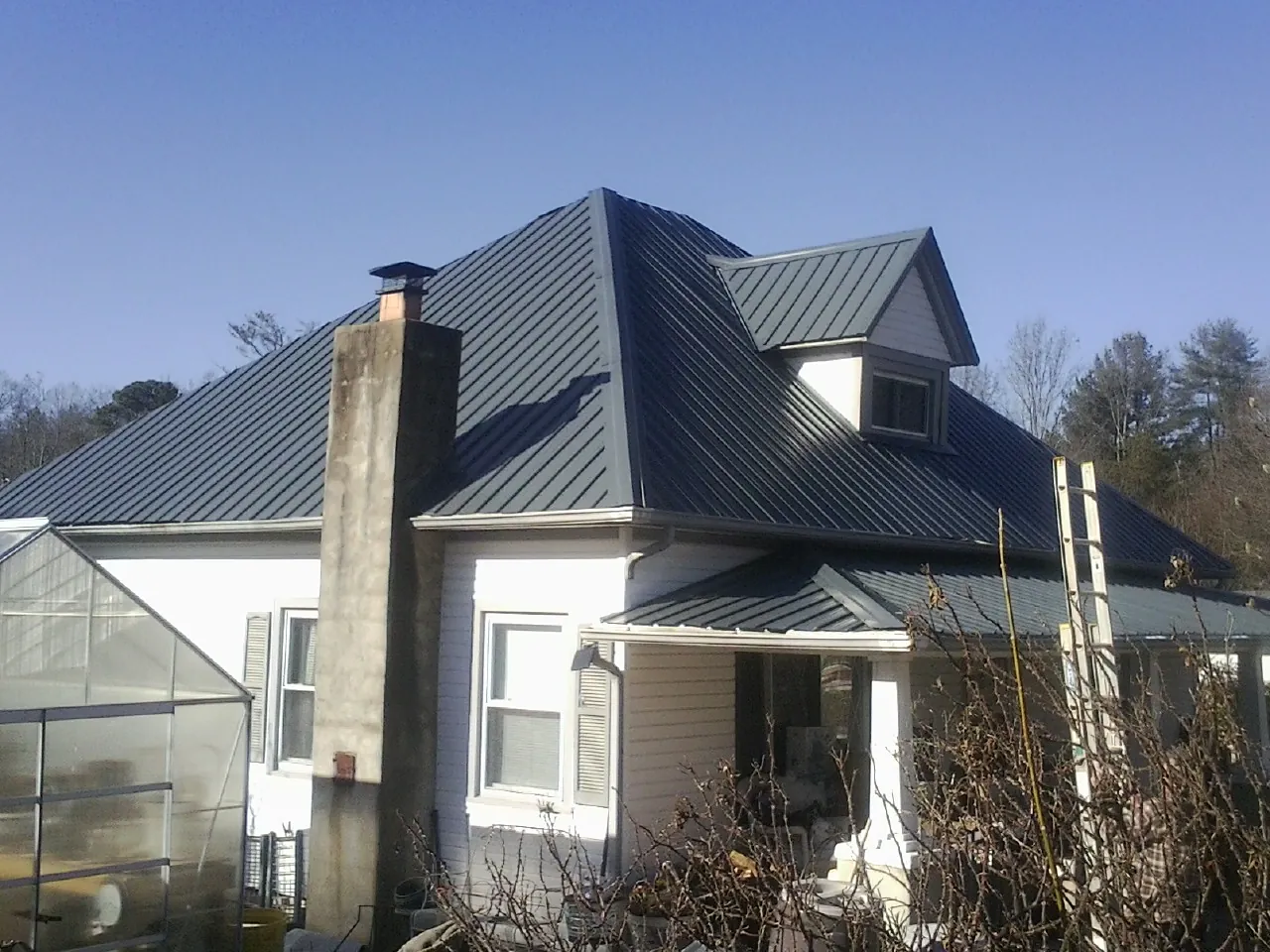 Dark blue standing seam metal roof on a white farmhouse with dormer — Slate & Tile Roof Repair by Roofing Brothers in West Chesterfield