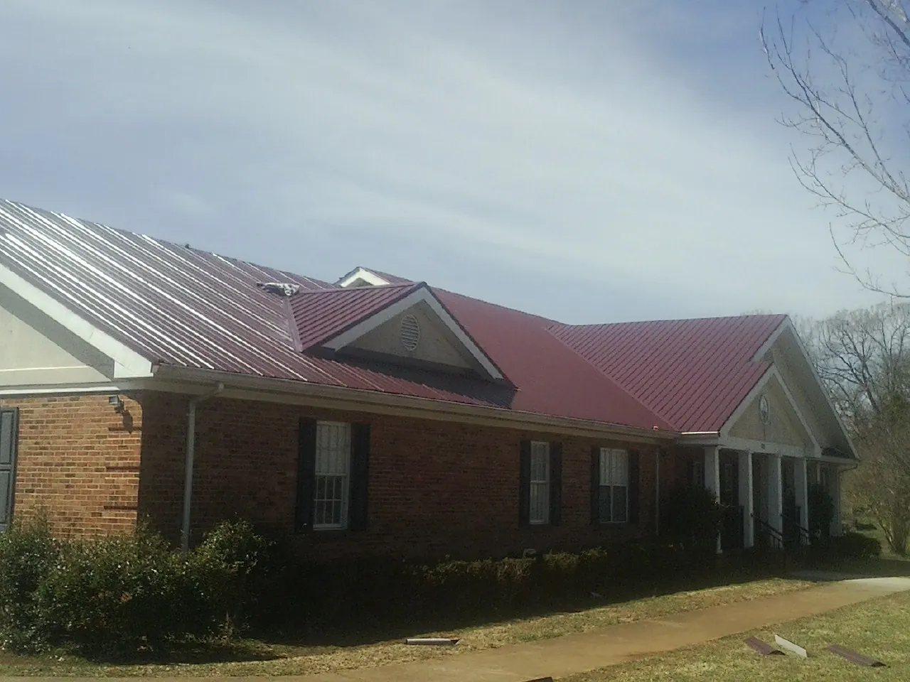 Red metal roof with gabled entries on a long brick building, from a Hail Damage Roof Repair job in West Chesterfield